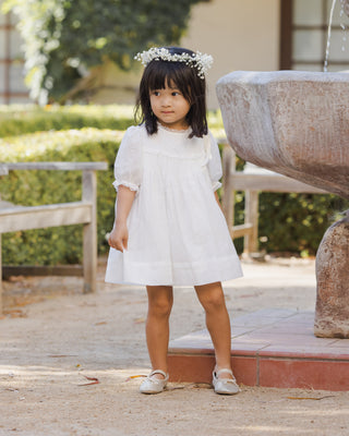 Noralee Penelope Dress - White
Young girl in a white dress standing outdoors near a fountain