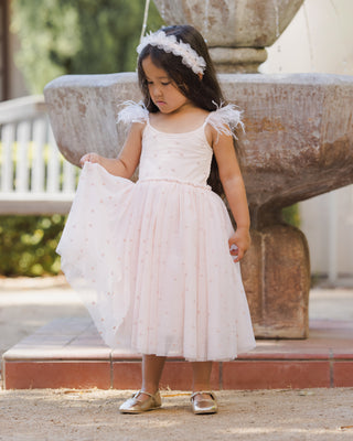 Noralee Poppy Dress - Blush Young girl in a white dress with floral headband standing outdoors near a stone fountain.