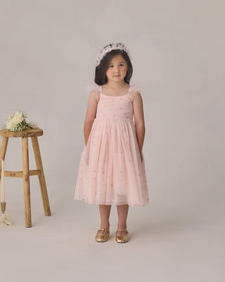 Noralee Poppy Dress - Blush
Young girl in a pink dress standing next to a wooden stool on a plain background