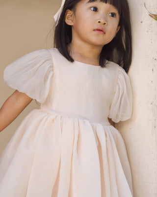 Noralee Sofia Dress - Blush
Young girl wearing a white dress with puffed sleeves against a neutral background