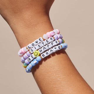 Little Words Project Bracelet - Kids: Be Happy
Stack of colorful beaded bracelets with motivational phrases on a wrist against a beige background