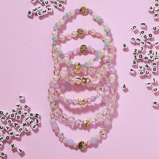 Little Words Project Bracelet - Beaded Charm
Set of beaded necklaces with charms on a pink background with scattered letters.