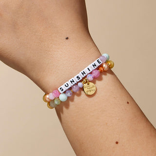 Little Words Project Bracelet - Sunshine
Multicolored beaded bracelet with 'SUNSHINE' charm on a wrist against a beige background