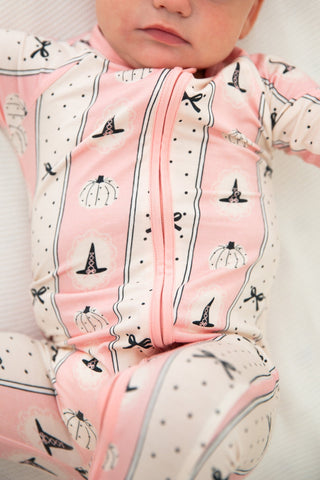 In My Jammers Zipper Romper - Pretty Little Pumpkin
A close-up of a baby wearing a pink and cream footed sleeper with a black witch hat and pumpkin print, lying on a white blanket.
