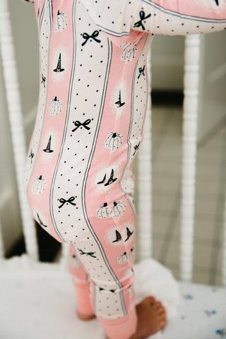 In My Jammers Zipper Romper - Pretty Little Pumpkin
Pink and white patterned baby leggings with black bows, pumpkins, and polka dots, shown on a child standing on a white blanket.