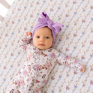 Posh Peanut Ruffled Zippered Footie - Mariselle
Baby in a floral outfit and purple headband lying on a floral blanket