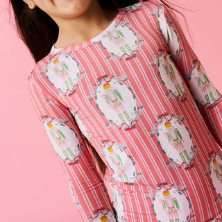 Posh Peanut Classic Pajama Set - Sable 
Close-up of a person wearing a pink outfit with nutcracker pattern on a pink background