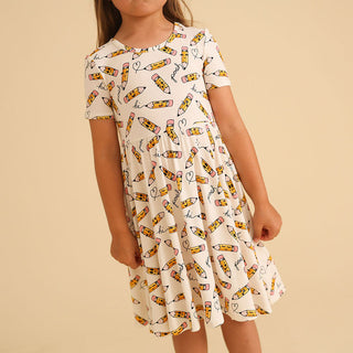 Posh Peanut Posh Pencils Ruffled Twirl Dress Child wearing a dress with pencil pattern on a beige background