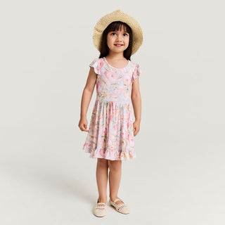 Girl wearing a Posh Peanut Ruffled Twirl Dress in Rose Dreams, featuring ruffles and a playful, twirling design in a cozy setting.