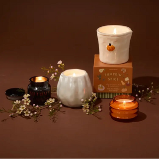 Paddywax White Metallic Pumpkin Candle - Flaming Pumpkin
A styled product display featuring a white ceramic candle holder with a small orange pumpkin detail, a lit white candle in a ribbed vase, a lit amber glass candle, and a brown box labeled 'Pumpkin Spice'.