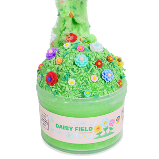 Peachybbies Cloud Slime - Daisy Field
A green slime product in a clear round tub with a pink label reading 'DAISY FIELD'. The lid is covered in bright green shredded material and decorated with small colorful flower appliqués, with more green slime piled on top against a white background.