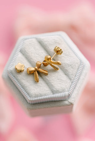 Pierced Co. Classic Bows Earrings
Gold bow-shaped earrings in a hexagonal jewelry box with a pink background