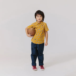 Blue Rooster Boys Jack Shirt - Flying Footballs Child wearing a yellow patterned shirt and dark pants, holding a basketball on a plain background