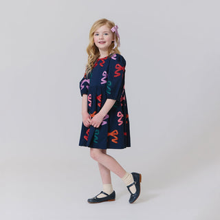 Pink Chicken Girls Brooke Dress - Multi Bow Applique
Young girl wearing a dark blue dress with colorful abstract patterns on a plain background