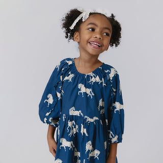 Pink Chicken Girls Katya Dress - Wild Horses
Young girl wearing a blue dress with horse patterns against a plain background