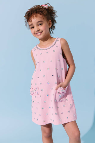 Pink denim dress with a heart-shaped crystal embellishment and a bow, designed by Lola & the Boys, showcased on a dress form.