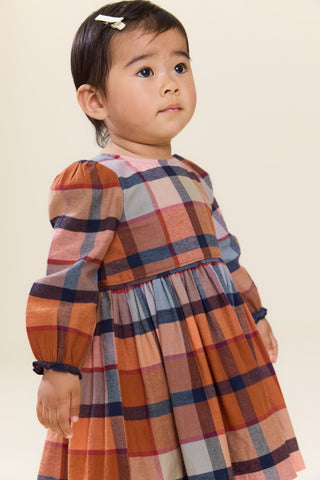 Pink Chicken Baby Girls Mae Dress Set - Hayride Plaid
A toddler girl wearing a long-sleeve plaid dress in rust orange, navy blue, and light gray, photographed against a plain beige studio background.