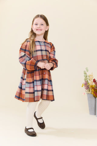Pink Chicken Girls Mae Dress - Hayride Plaid
A young girl with long light brown hair stands against a warm cream background wearing a long-sleeve plaid dress in orange, red, blue, and beige tones, paired with cream tights and dark leopard-print shoes.