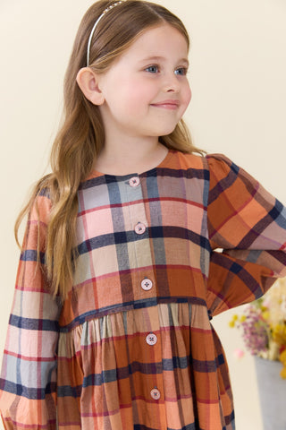 Pink Chicken Girls Mae Dress - Hayride Plaid
A young girl with long light brown hair wearing a long-sleeve plaid dress in orange, beige, navy, and pink, with a white headband, photographed against a soft cream background.