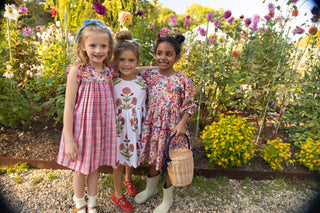 Pink Chicken Girls Maribelle Dress - Burgundy Sketched Floral
Three young girls in dresses standing in a garden with flowers and plants.