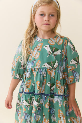 Pink Chicken Girls Maribelle Dress - Green Butterflies
A young girl with blonde hair wearing a green tiered dress with a colorful butterfly print, photographed against a plain beige background.