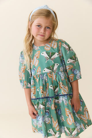 Pink Chicken Girls Maribelle Dress - Green Butterflies
A young girl with blonde hair wearing a tiered green dress with a butterfly print and a light blue headband, standing against a plain beige background.