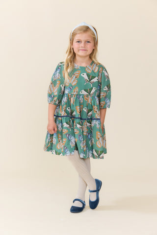 Pink Chicken Girls Maribelle Dress - Green Butterflies
A young girl stands against a plain beige studio background wearing a green tiered dress with a colorful butterfly print, white tights, navy shoes, and a white headband.