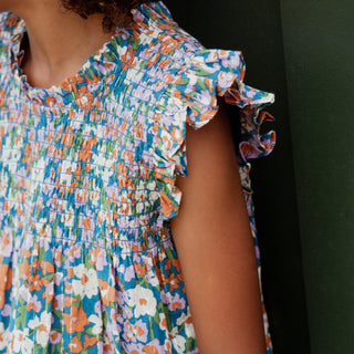 Pink Chicken Girls Stevie Dress - True Blue Sketched Floral
Close-up of a child wearing a smocked floral dress with ruffled sleeves, featuring a multicolor print of orange, white, and purple flowers on a blue background.