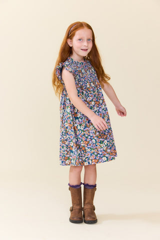 Pink Chicken Girls Stevie Dress - True Blue Sketched Floral\
A young girl with long red hair stands against a plain beige studio background wearing a sleeveless knee-length dress with a dense multicolor floral print and brown boots.