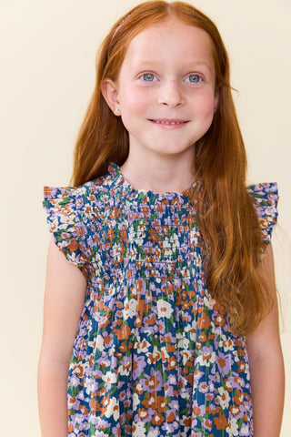 Pink Chicken Girls Stevie Dress - True Blue Sketched Floral
A young girl with long red hair and blue eyes wearing a colorful floral smocked dress, photographed against a plain cream background.