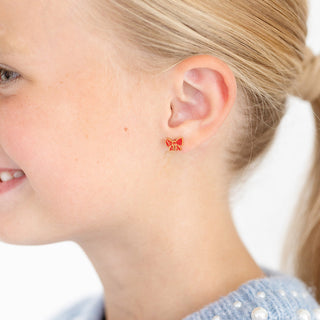 Pip Pop Post Earrings - Red Enamel Bow
Close-up of a child wearing butterfly-shaped earrings with a visible brand logo.