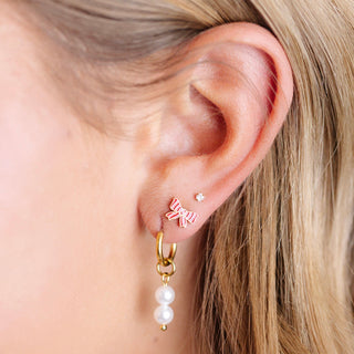 Pip Pop Post Earrings - Striped Bow
Close-up of an ear wearing a gold hoop earring with pearl drop and a bow-shaped earring.