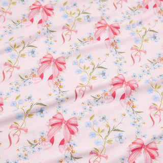 Posh Peanut  - Harriet
A close-up of a light pink fabric with a repeating pattern of pink satin bows, small blue forget-me-nots, and green stems.