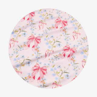 Posh Peanut - Harriet
A circular fabric sample featuring a delicate floral print with pink bows, small blue flowers, and green leaves on a pale pink background.