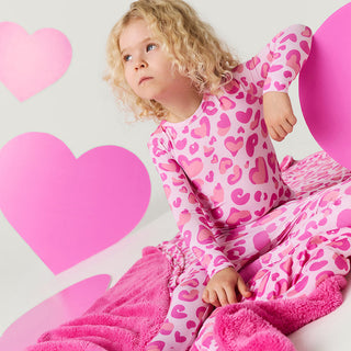 Posh Peanut Classic Pajama Set - Love Leopard
Child wearing a pink heart-patterned onesie with pink hearts in the background