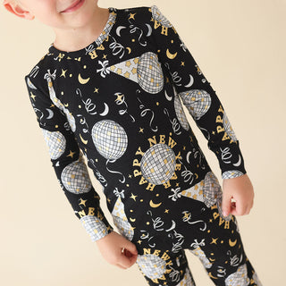 Posh Peanut Classic Pajama Set - Midnight Bash
Child wearing a black long-sleeve shirt with New Year's Eve-themed print on a beige background