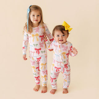 Posh Peanut Classic Pajama Set - Shawna
Posh Peanut Convertible One Piece - Shawna
Two children wearing matching pajamas with bow patterns on a beige background