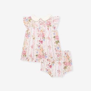 Posh Peanut Collared Smocked Ruffled Dress Bummie Set - Janey
A baby girl's two-piece outfit featuring a short-sleeve smocked dress with a cream Peter Pan collar and matching bloomers, both decorated with a delicate pink, red, and blue floral print on a cream background.