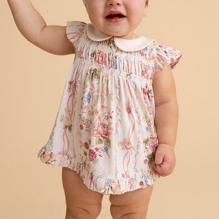 Posh Peanut Collared Smocked Ruffled Dress Bummie Set - Janey
A baby wearing a short-sleeve floral romper with a Peter Pan collar, photographed against a solid beige background.