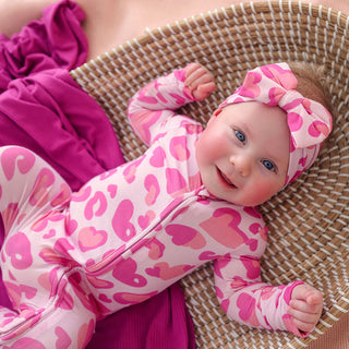 Posh Peanut Convertible One Piece - Love Leopard
Baby in a pink heart-patterned outfit lying on a woven surface