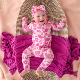 Posh Peanut Convertible One Piece - Love Leopard
Baby in pink leopard print outfit and headband sitting on a textured surface with pink and purple blankets.