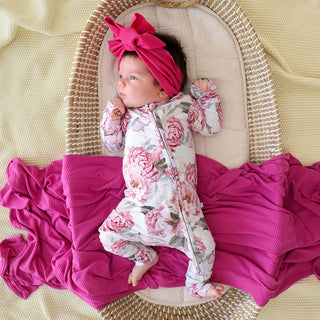 Posh Peanut Convertible One Piece - Lucienne
Newborn baby in a floral outfit and pink headband lying in a Moses basket with pink blankets.