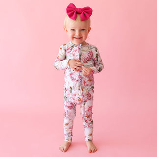 Posh Peanut Convertible One Piece - Lucienne
Child wearing a floral onesie with a pink bow on a pink background