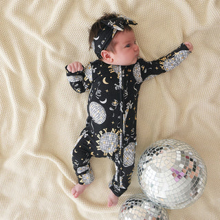 Posh Peanut Convertible One Piece - Midnight Bash
Baby wearing a black onesie with space-themed print, lying on a beige blanket with disco balls.