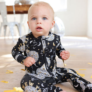 Posh Peanut Convertible One Piece - Midnight Bash
Baby wearing a black onesie with white patterns sitting on a wooden floor.