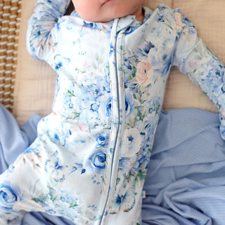 Posh Peanut Convertible One Piece - Trista
Baby in a floral onesie with blue roses and butterflies on a beige couch.