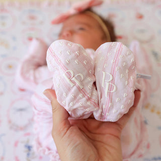 Posh Peanut Footie Ruffled Zippered One Piece - Remi
Heart-shaped pink pouch with initials held by a hand, with a baby in the background.