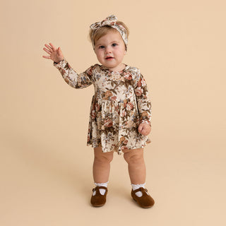 Posh Peanut Long Sleeve Twirl Bodysuit Dress - Dauphine
A toddler girl wearing a long-sleeve floral dress, matching headband, white socks, and brown Mary Jane shoes, standing against a solid beige studio background.
