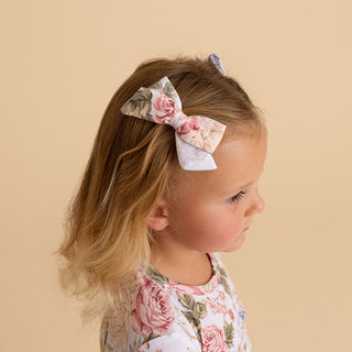 Posh Peanut Mini Bow Hair Clips - Kristiana
A young girl in profile wearing a floral bow headband and a matching floral top, set against a solid beige background.