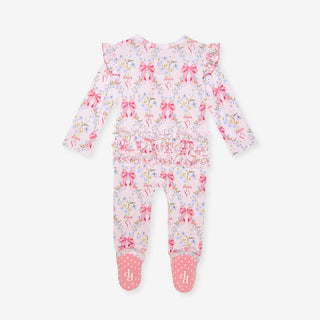Posh Peanut Picot Footie Ruffled Zippered One Piece - Harriet
A baby long-sleeve footed one-piece romper in a light pink floral print with pink bows, ruffled shoulders, and pink polka-dot toe caps on a light gray background.
